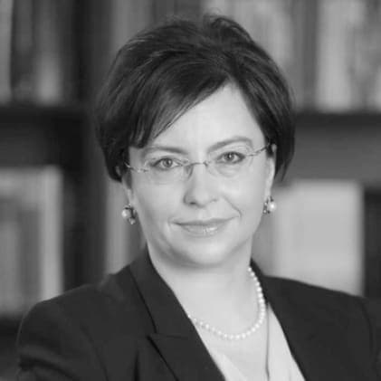 A woman wearing glasses and a suit in front of a bookshelf